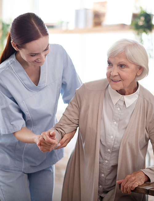 Helping to walk. Caregiver wearing uniform smiling while helping aged woman to walk